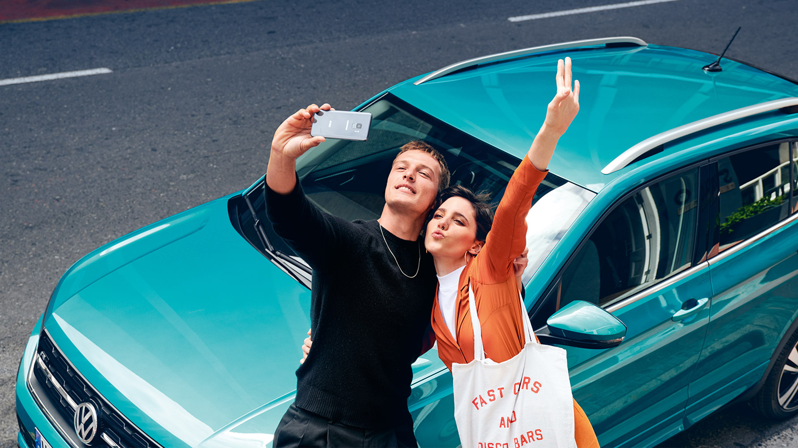 Ein Pärchen macht ein Selfie vor einem türkisenen VW T-Cross