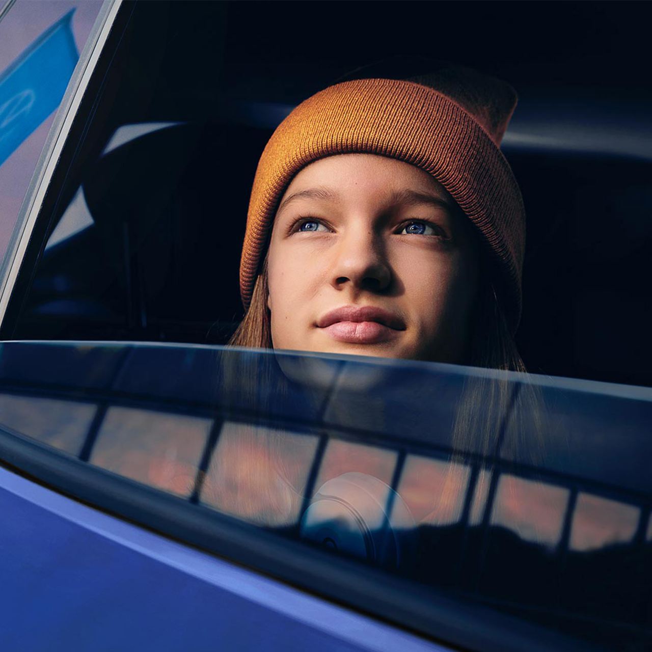 Eine junge Frau schaut verträumt aus dem offenen Fenster eines Autos in den Himmel – Versicherungen